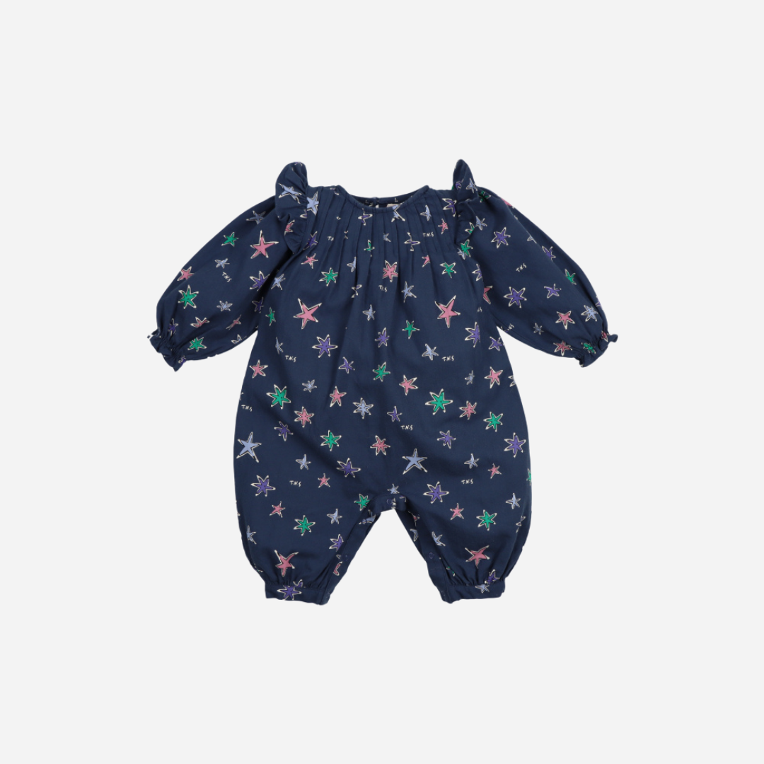 Sold at Bombon shop, this baby girl romper by The New Society features a navy background with a colorful star print, puffed long sleeves, ruffle shoulder details, and gathered cuffs for a whimsical and comfortable all-in-one outfit. front
