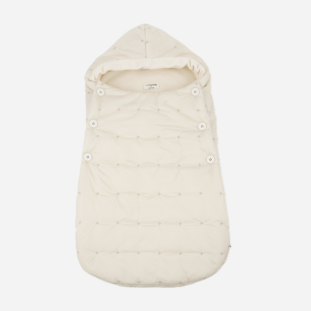 Sold at Bombon shop, designed by 1+ in the family — cream-colored quilted baby nest with hood and side button closure, crafted for warmth and comfort. front