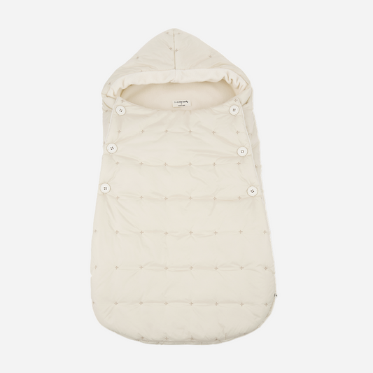 Sold at Bombon shop, designed by 1+ in the family — cream-colored quilted baby nest with hood and side button closure, crafted for warmth and comfort. front