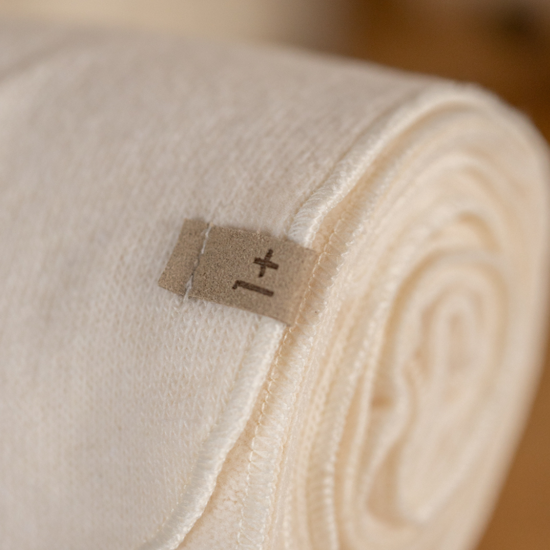 Sold at Bombon shop, designed by 1+ in the family — rolled ecru baby blanket with tie detail and soft knit texture. zoom