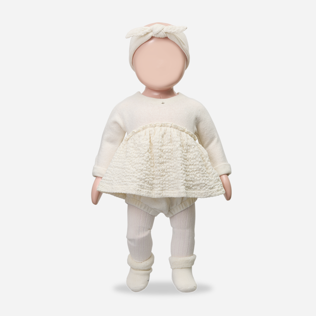 Baby doll wearing a cream outfit with a textured skirt on a white background