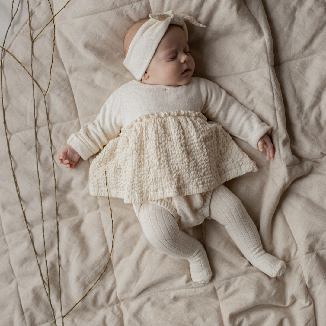 Sold at Bombon shop, designed by 1+ in the family — ecru ribbed baby tights with enclosed feet, photographed flat on white background. model