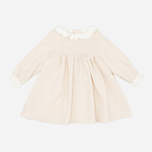 Sold at Bombon shop, designed by Fina Ejerique, a beige corduroy baby dress with smocked bodice, white ruffle collar, and long sleeves. front