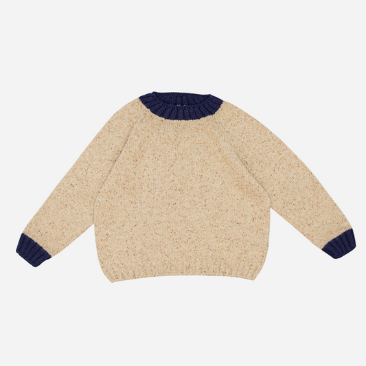 Sold at Bombon shop, designed by Fina Ejerique, a beige knit baby sweater with navy ribbed collar and cuffs, styled to pair with the multicolor checkered shirt. front