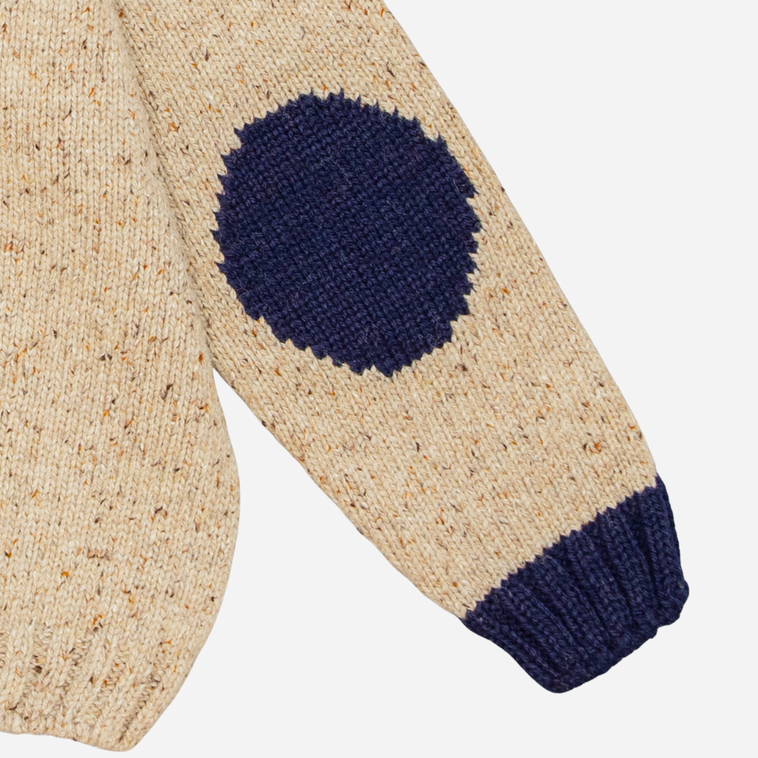 Sold at Bombon shop, designed by Fina Ejerique, a beige knit baby sweater with navy ribbed collar and cuffs, styled to pair with the multicolor checkered shirt. sleeve