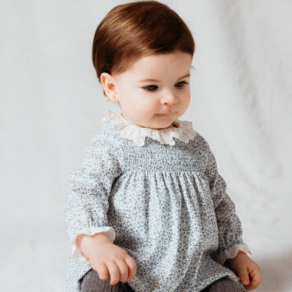Sold at Bombon shop, designed by Fina Ejerique, a white floral viyella baby dress with smocked bodice, ruffle collar, and long sleeves. model