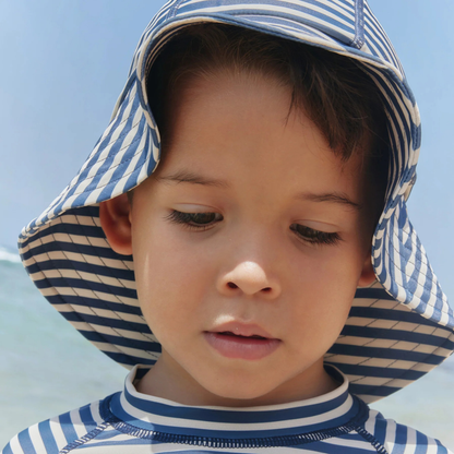 Sold at Bombon Shop, designed by Wheat, blue stripe UV sun hat in recycled fabric with soft brim and navy striped pattern.