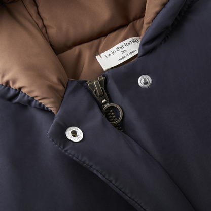 Sold at Bombon shop, designed by 1+ in the family — navy baby puffer jacket with brown lining, hood, front snaps, and patch pockets, laid flat on white background. zoom