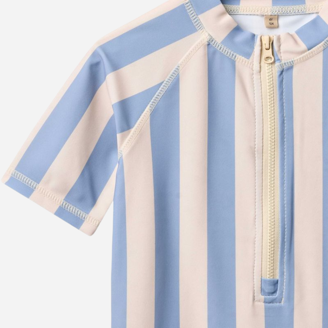 Sold at Bombon Shop, designed by Wheat, blue sky stripe short sleeve one-piece swimsuit in recycled fabric with vertical stripes and front zip closure.