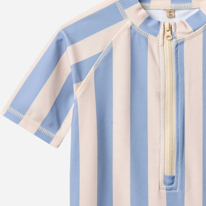 Sold at Bombon Shop, designed by Wheat, blue sky stripe short sleeve one-piece swimsuit in recycled fabric with vertical stripes and front zip closure.
