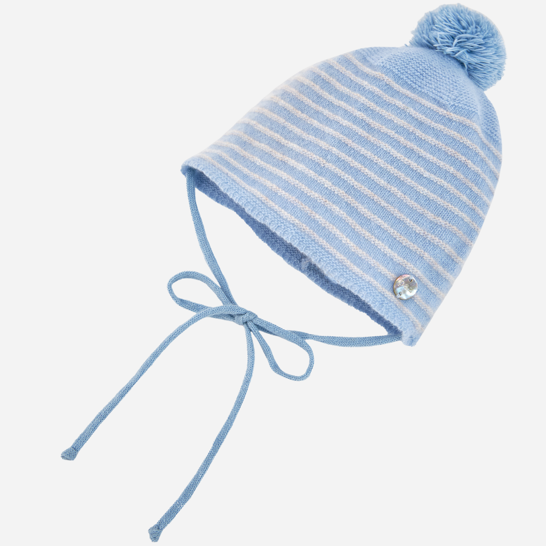 Sold at Bombon shop, designed by Paz Rodriguez. Baby cashmere hat in pale blue with pompom and ties, shown from front view.
