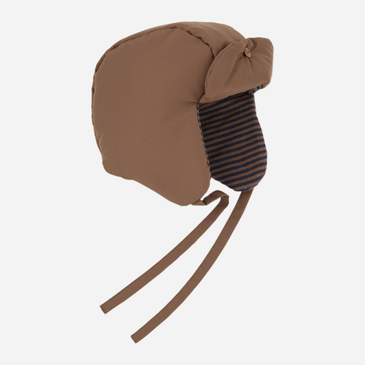 Sold at Bombon shop, designed by 1+ in the family — brown padded baby hat with navy striped ear flaps and chin ties, photographed from the side on a white background. front