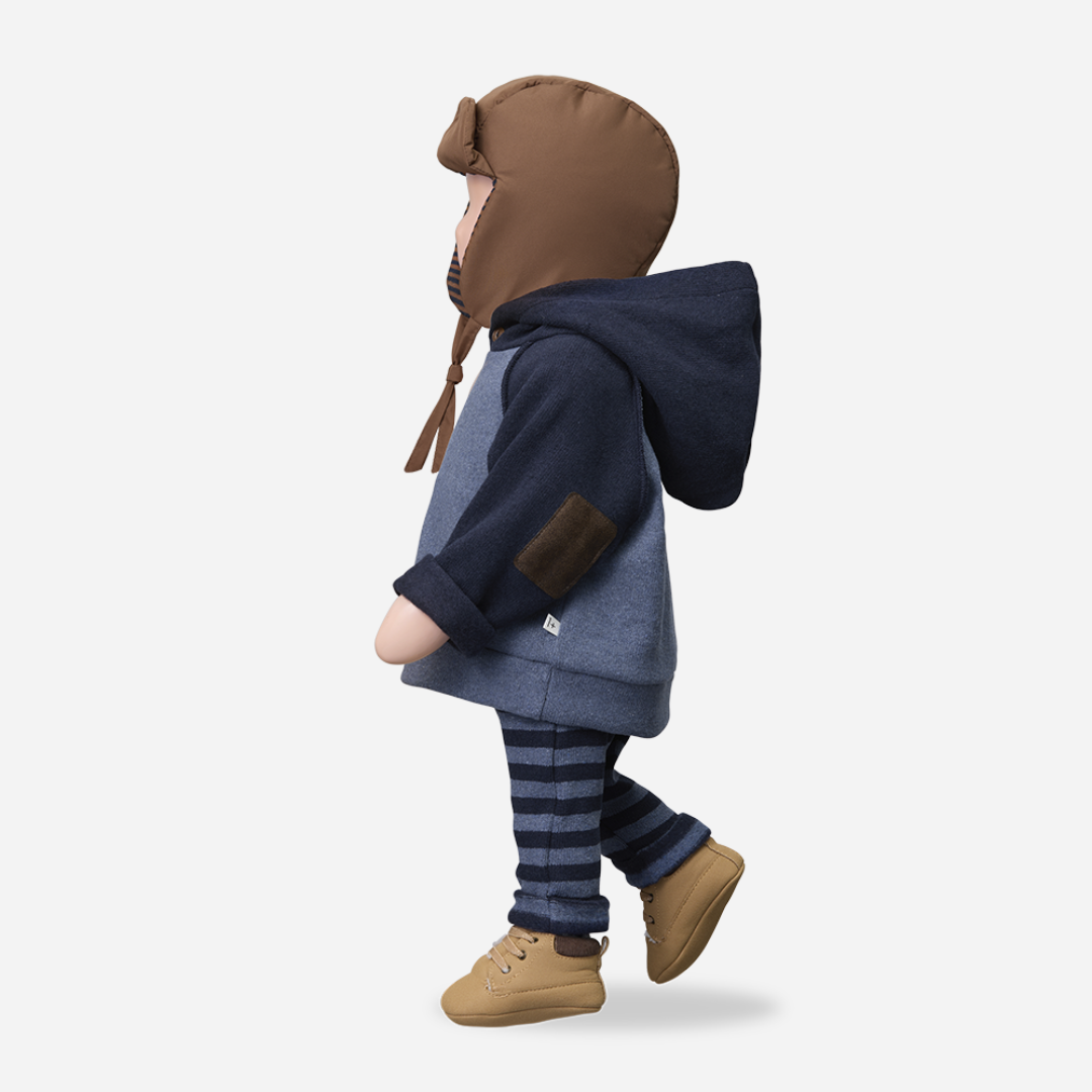 Sold at Bombon shop, designed by 1+ in the family — brown padded baby hat with navy striped ear flaps and chin ties, photographed from the side on a white background. mannequin