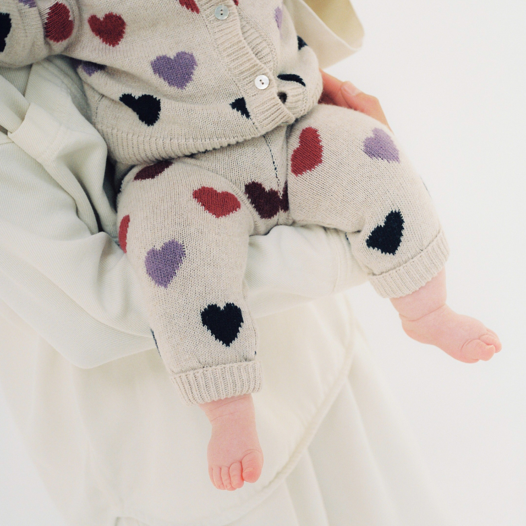 Sold at Bombon Shop, these baby girl knit pants by The New Society come in a soft beige hue with an allover multicolor heart pattern and ribbed trims. model