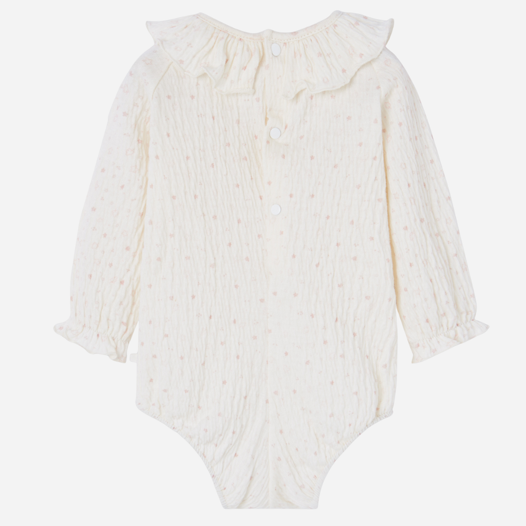 Sold at Bombon shop, designed by Paz Rodriguez. Cream floral muslin baby bodysuit with ruffle collar paired with pink knit overalls featuring front pocket and button straps.