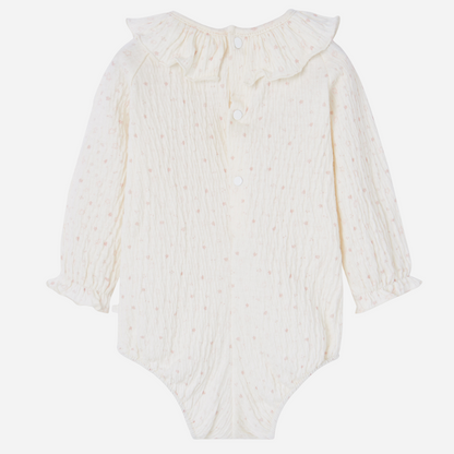 Sold at Bombon shop, designed by Paz Rodriguez. Cream floral muslin baby bodysuit with ruffle collar paired with pink knit overalls featuring front pocket and button straps.