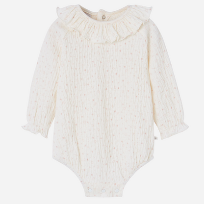Sold at Bombon shop, designed by Paz Rodriguez. Cream floral muslin baby bodysuit with ruffle collar paired with pink knit overalls featuring front pocket and button straps.