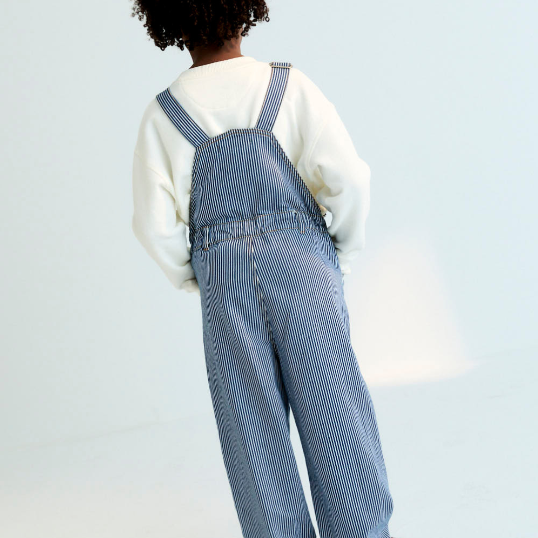 Sold at Bombon Shop, these unisex overalls by The New Society are made from a striped denim with a vintage wash, featuring adjustable shoulder straps, side button closures, and patch pockets for a timeless, relaxed silhouette. model, back
