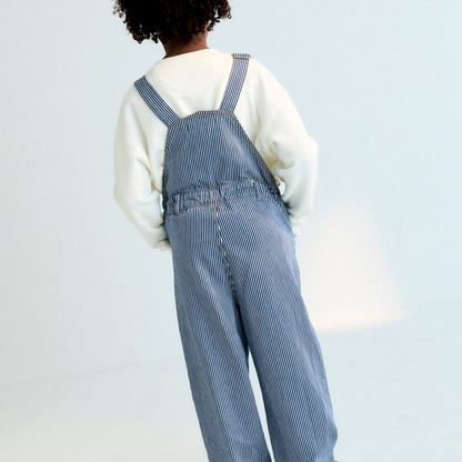 Sold at Bombon Shop, these unisex overalls by The New Society are made from a striped denim with a vintage wash, featuring adjustable shoulder straps, side button closures, and patch pockets for a timeless, relaxed silhouette. model, back