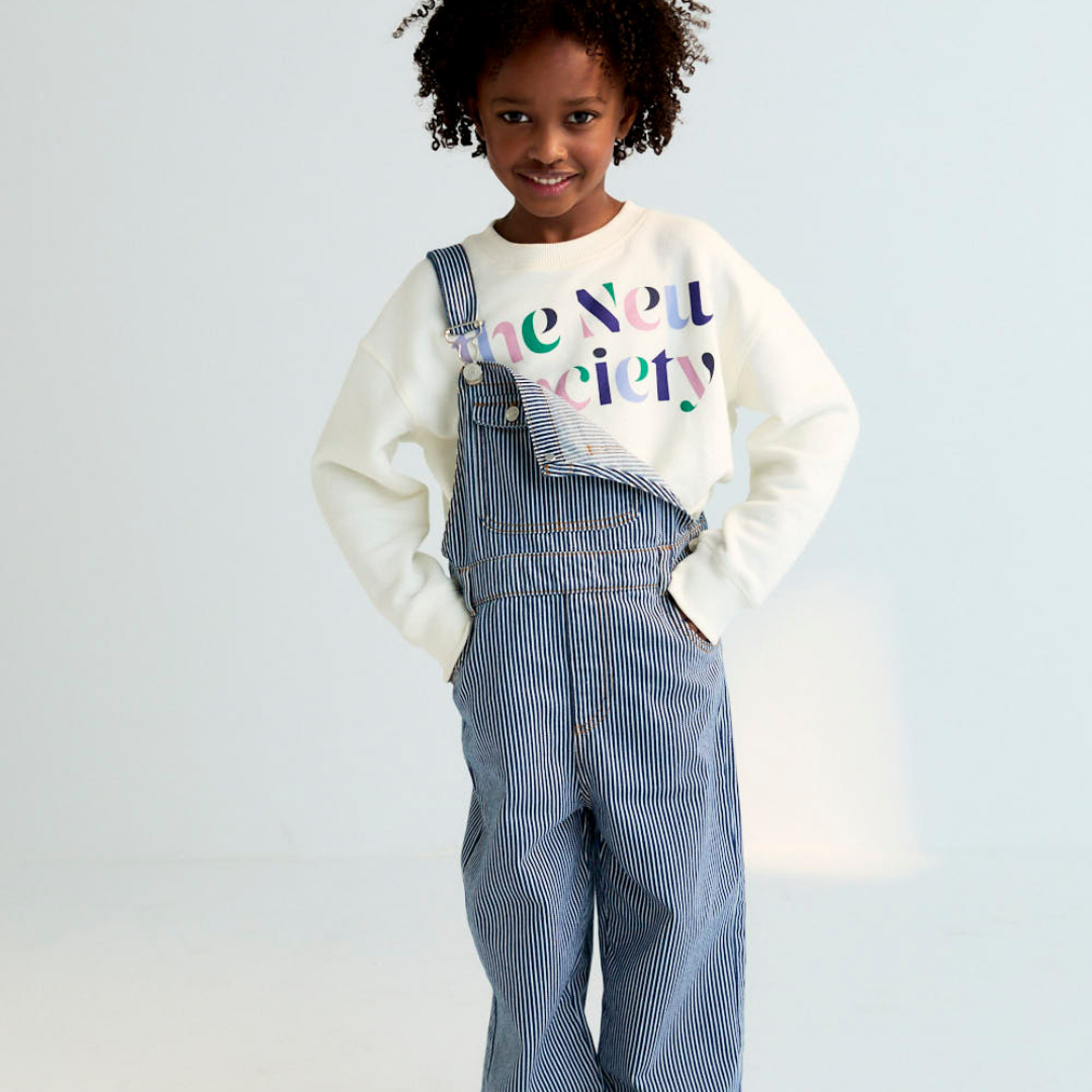 Sold at Bombon Shop, these unisex overalls by The New Society are made from a striped denim with a vintage wash, featuring adjustable shoulder straps, side button closures, and patch pockets for a timeless, relaxed silhouette. model