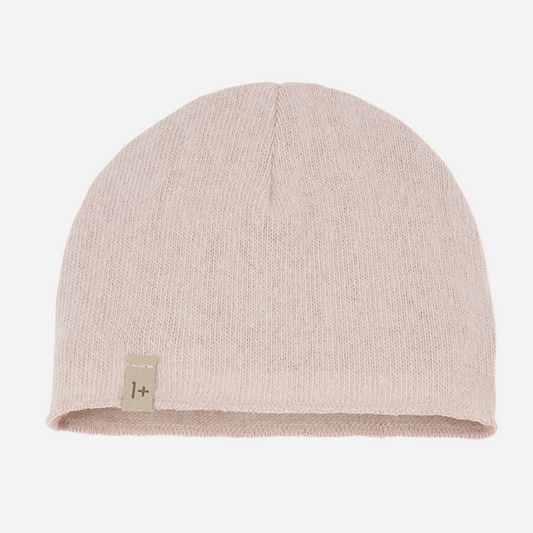 Sold at Bombon shop, designed by 1+ in the family — nude pink knit baby beanie with stitched logo tag, laid flat on a white background