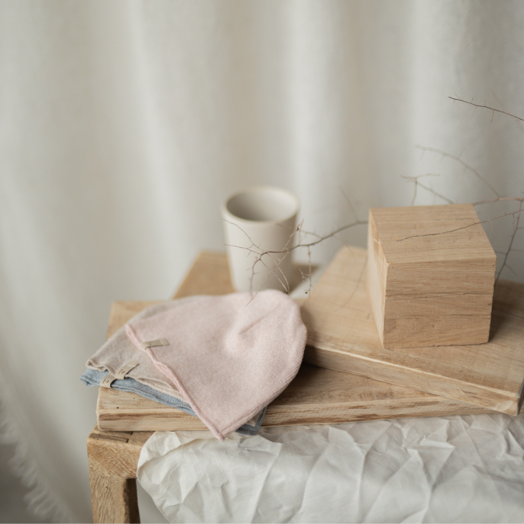 Sold at Bombon shop, designed by 1+ in the family — nude pink knit baby beanie with stitched logo tag, laid flat on a white background. lifestyle