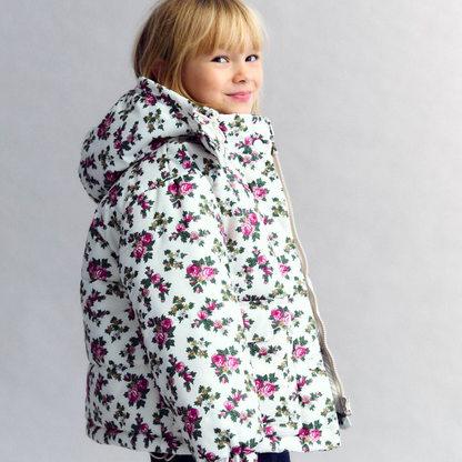 Sold at Bombon shop, this girls’ puffer jacket by The New Society features an all-over rose floral print on a cream base, complete with a hood, front pockets, and snap-button closure—combining warmth, function, and a touch of charm for cooler days. model