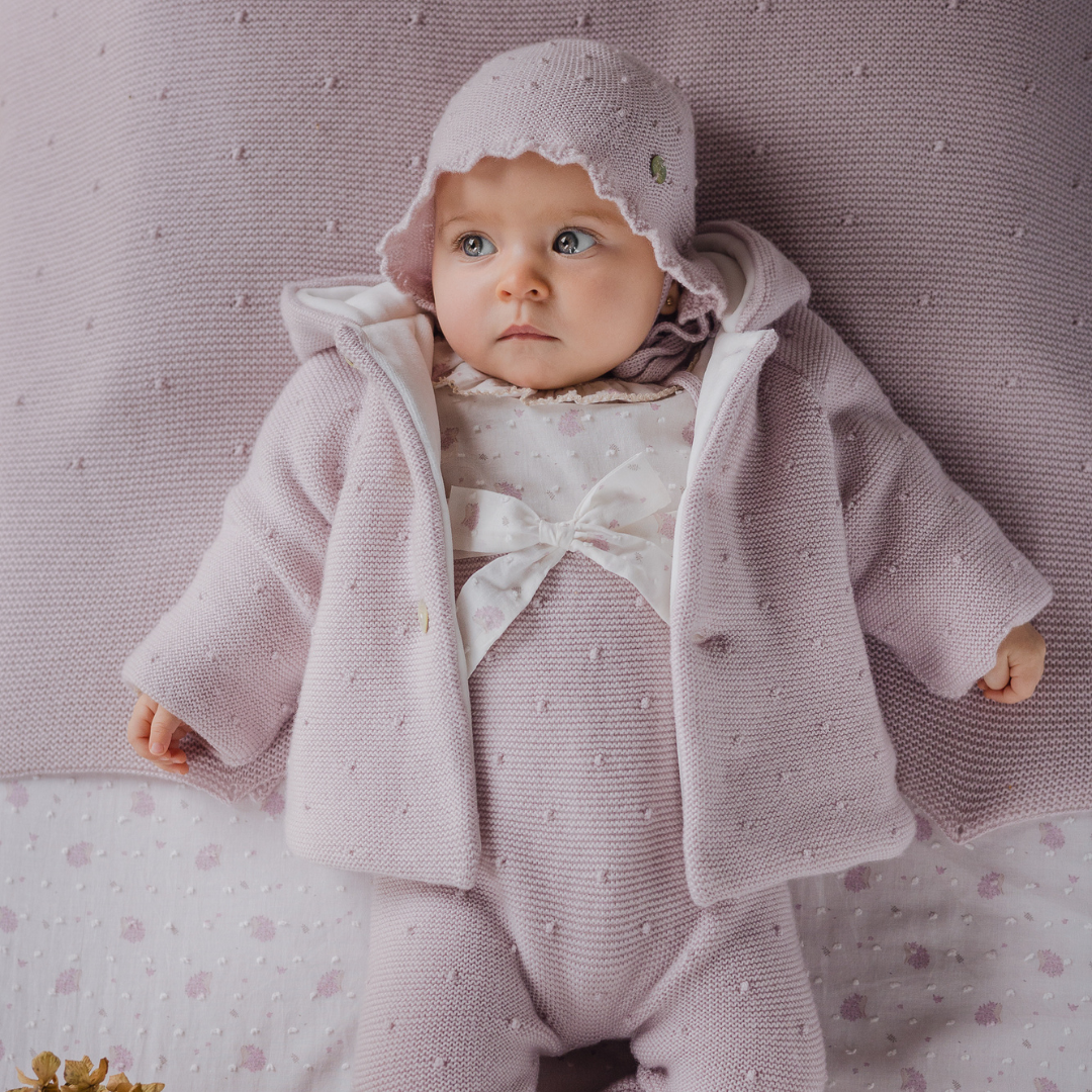Sold at Bombon shop, designed by Paz Rodriguez, light pink knit baby hat with scalloped brim, bobble texture, and tie closure under the chin.