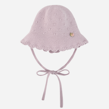 Sold at Bombon shop, designed by Paz Rodriguez, light pink knit baby hat with scalloped brim, bobble texture, and tie closure under the chin.