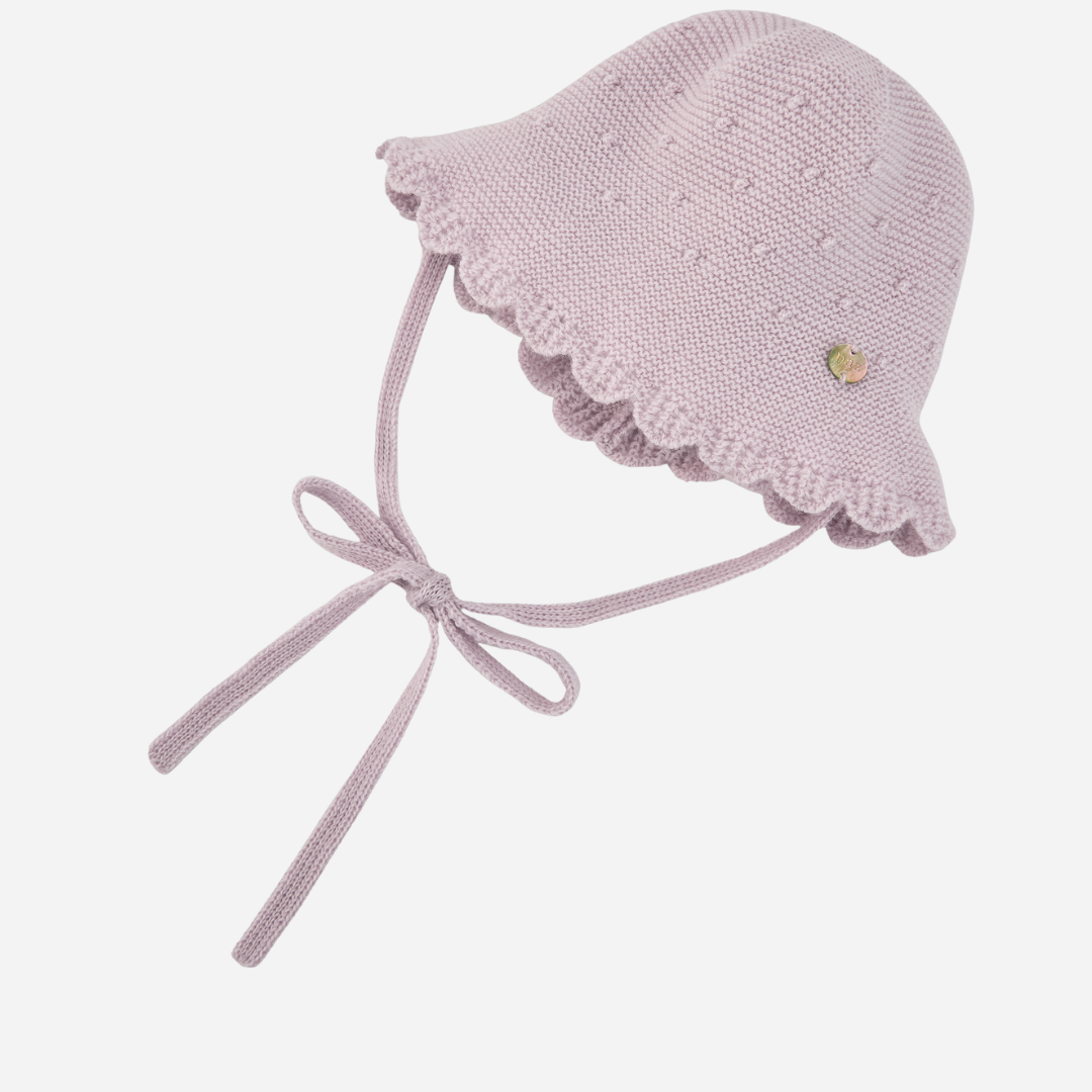 Sold at Bombon shop, designed by Paz Rodriguez, light pink knit baby hat with scalloped brim, bobble texture, and tie closure under the chin.