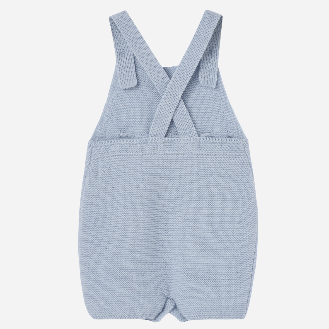 Sold at Bombon shop, designed by Paz Rodriguez. Light blue knitted baby overall with textured dots, waist bow, and button closures.