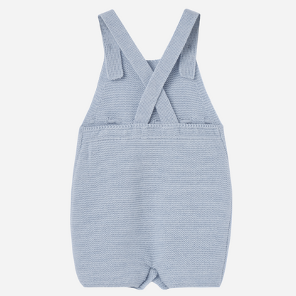 Sold at Bombon shop, designed by Paz Rodriguez. Light blue knitted baby overall with textured dots, waist bow, and button closures.