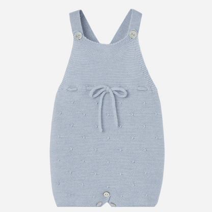 Sold at Bombon shop, designed by Paz Rodriguez. Light blue knitted baby overall with textured dots, waist bow, and button closures.