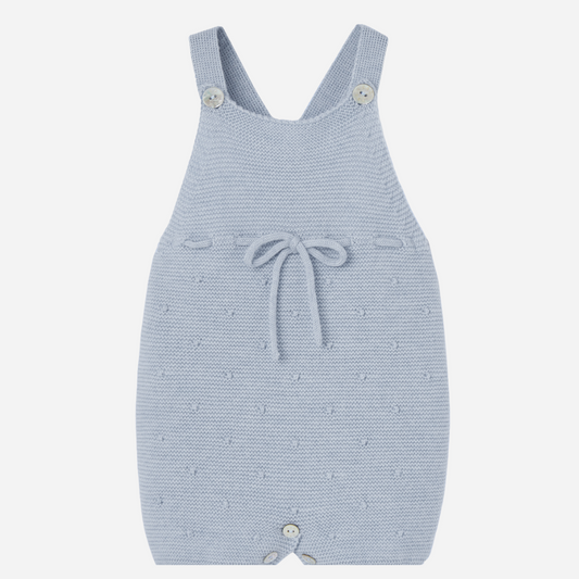 Sold at Bombon shop, designed by Paz Rodriguez. Light blue knitted baby overall with textured dots, waist bow, and button closures.