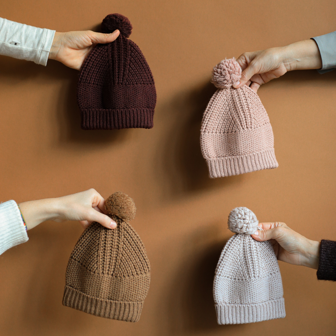 Sold at Bombon shop, designed by 1+ in the family — dark purple melanzana knit baby beanie with pom-pom and wide fold-over brim, displayed flat on a white background. lifestyle