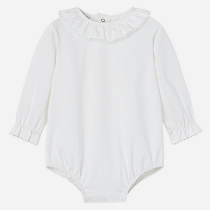 Sold at Bombon shop, designed by Paz Rodriguez. White baby bodysuit with long sleeves, ruffled collar, and lace-trimmed cuffs