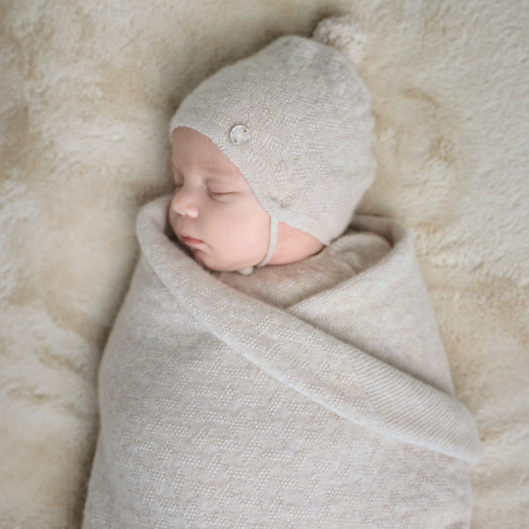 Sold at Bombon shop, designed by Paz Rodriguez. Beige knit baby blanket with delicate ribbing and textured detail, folded neatly