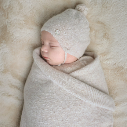 Sold at Bombon shop, designed by Paz Rodriguez. Beige knit baby blanket with delicate ribbing and textured detail, folded neatly