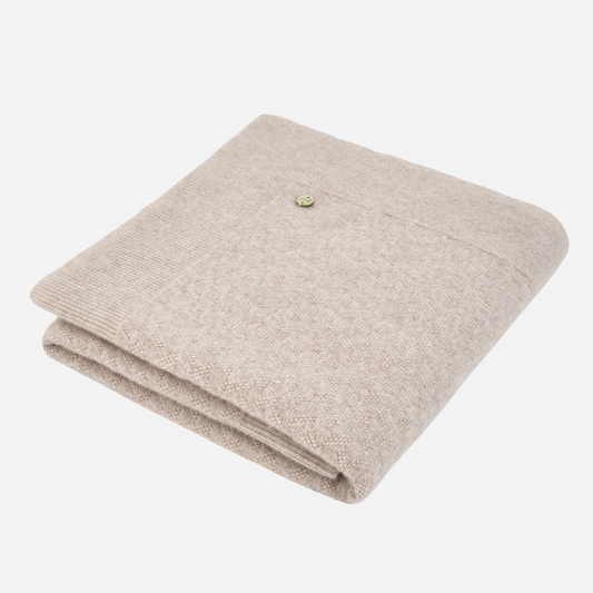 Sold at Bombon shop, designed by Paz Rodriguez. Beige knit baby blanket with delicate ribbing and textured detail, folded neatly
