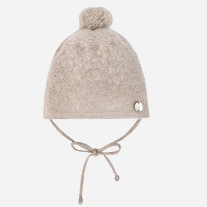 Sold at Bombon shop, designed by Paz Rodriguez. Beige knit baby hat with pompom and chin ties, perfect for cold weather.