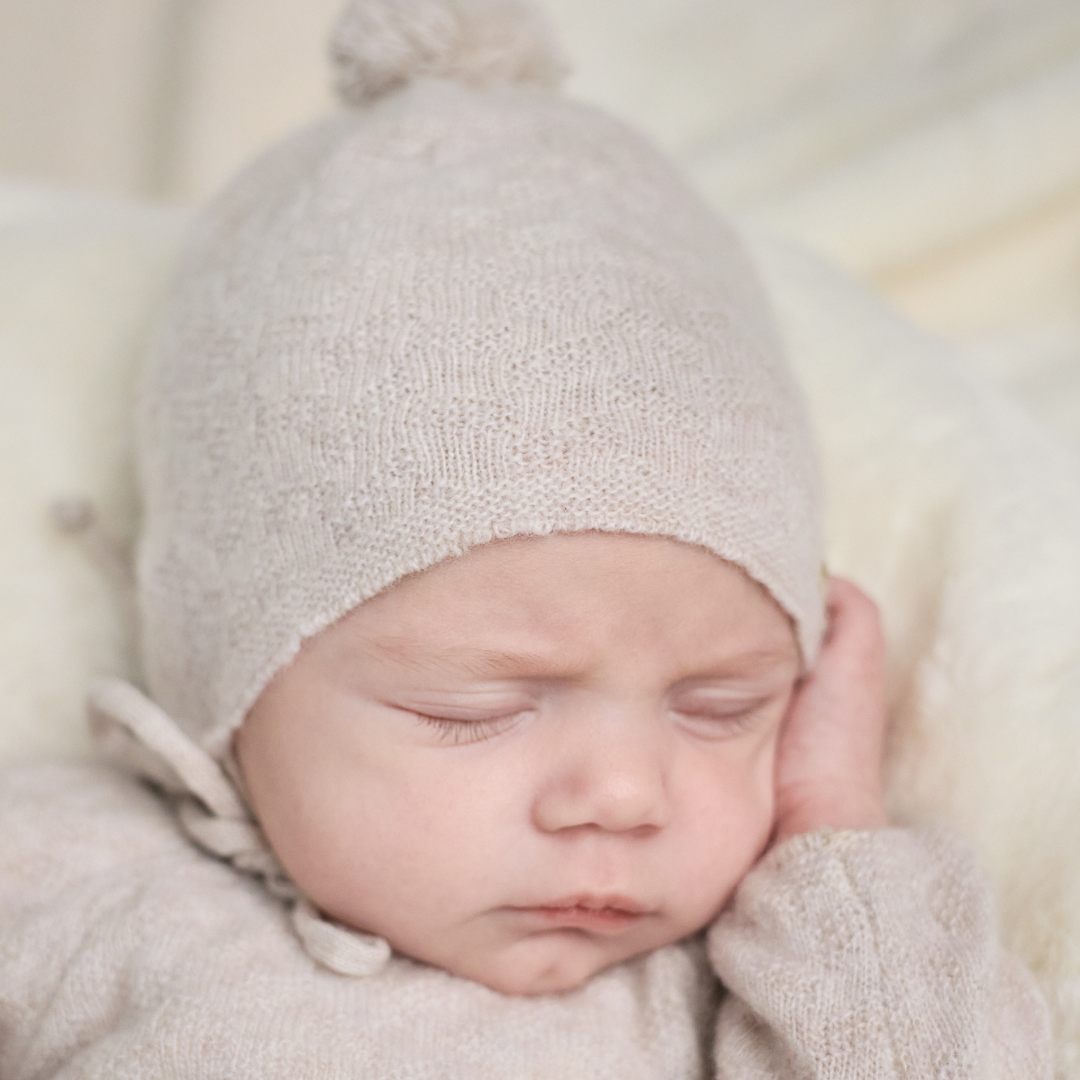 Sold at Bombon shop, designed by Paz Rodriguez. Beige knit baby hat with pompom and chin ties, perfect for cold weather.
