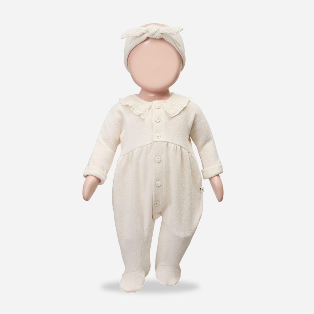 Baby doll wearing a cream-colored outfit with a matching headband on a white background