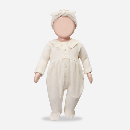 Baby doll wearing a cream-colored outfit with a matching headband on a white background