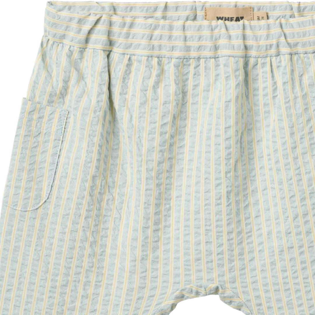 Sold at Bombon Shop, designed by Wheat, summer sky stripe organic cotton baby trousers with elastic waistband and soft blue vertical stripes.