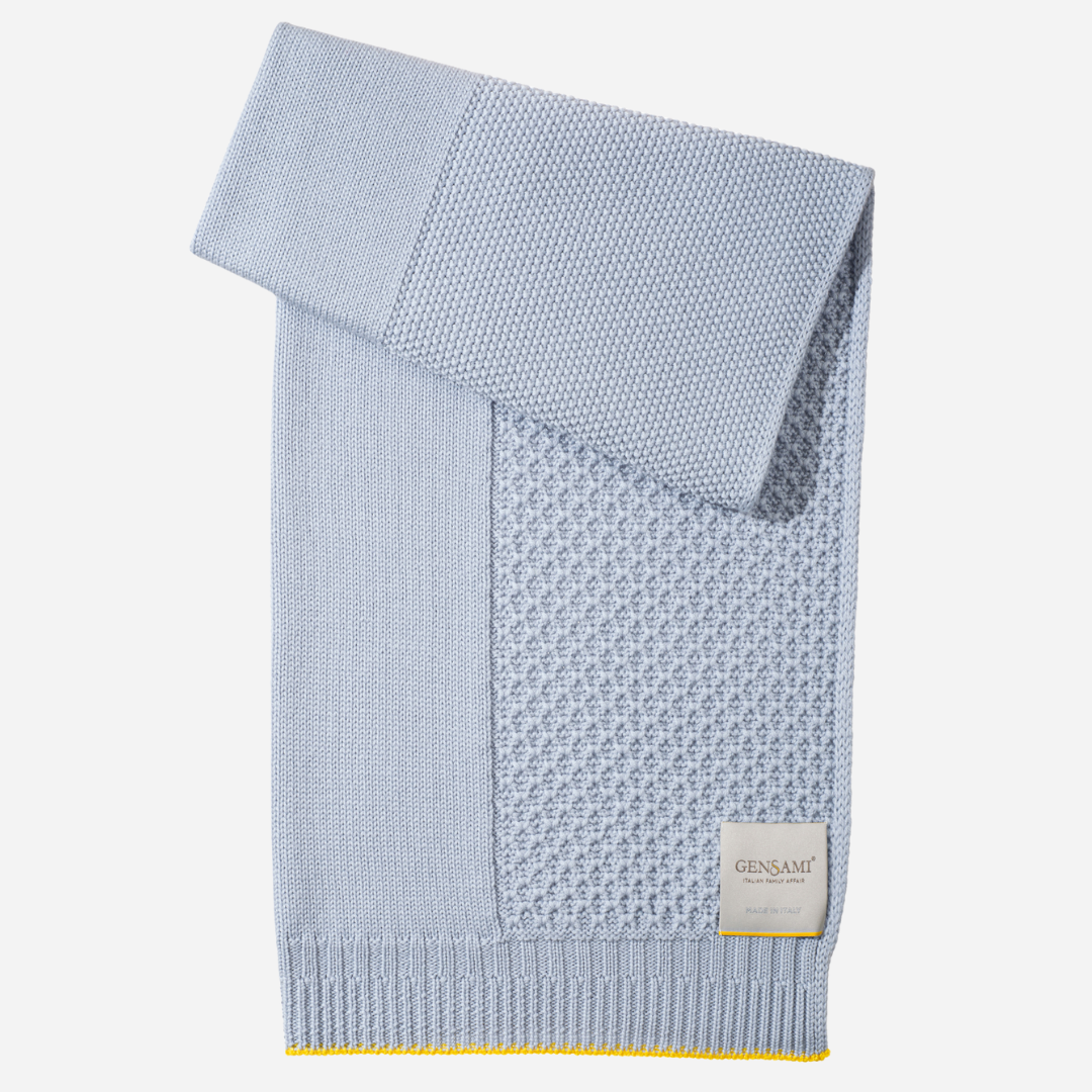 Sold at Bombon and designed by Gensami, a blue knit baby blanket with yellow edging, elegantly folded for gifting.