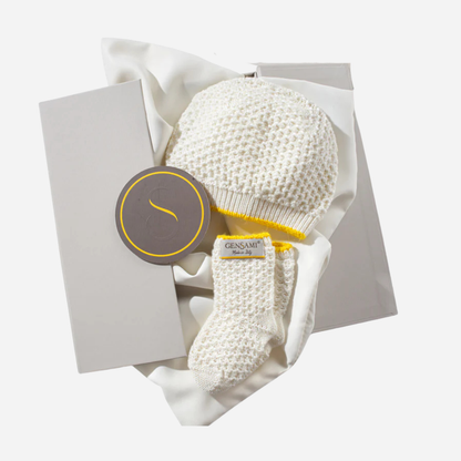 Sold at Bombon and designed by Gensami, an ivory newborn layette set including a knit jumpsuit, hat, booties, and blanket with yellow trim