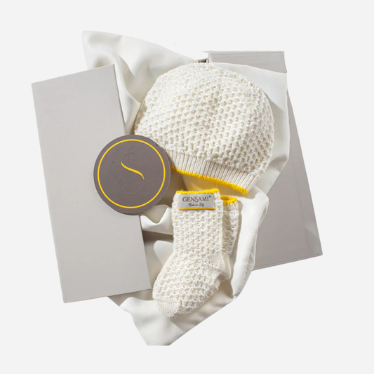 Sold at Bombon and designed by Gensami, an ivory knit baby hat and matching booties with yellow trim, crafted from soft cotton.