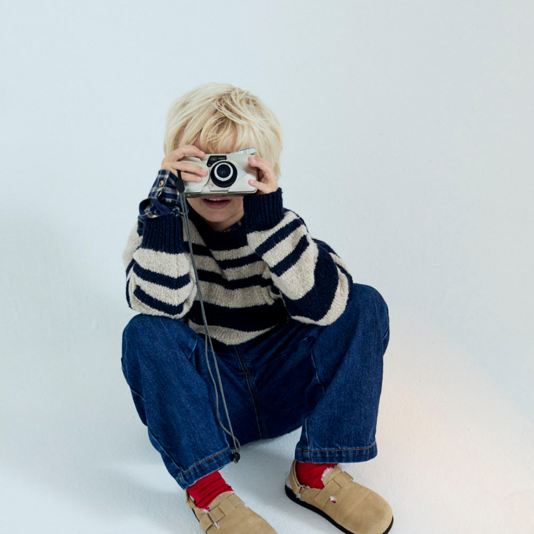Sold at Bombon shop, this kids' sweater by The New Society features classic navy and beige stripes in a soft knit fabric, with a round neckline, ribbed trims, and gold embroidered detail on the chest for a cozy and stylish everyday layer. model