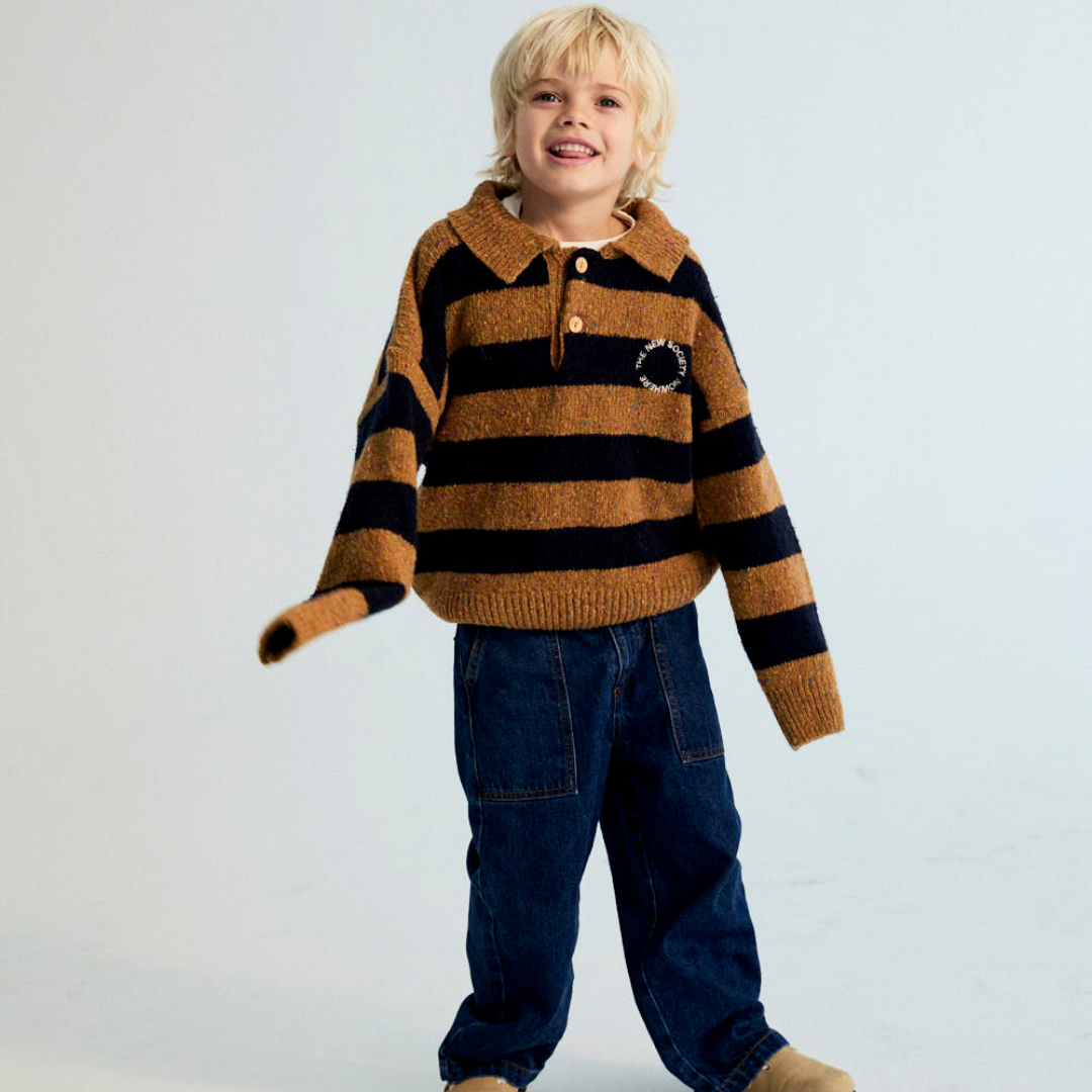 Sold at Bombon shop, this kids' knit polo sweater by The New Society features wide mustard and navy stripes, a classic collar with button placket, and a small embroidered chest logo—blending cozy comfort with a sporty, vintage-inspired look. model
