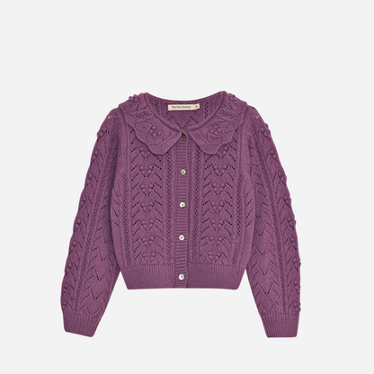 Sold at Bombon shop, this girls’ cardigan by The New Society features a rich lilac hue with an intricate pointelle knit pattern, scalloped Peter Pan collar, and front button closure—offering a refined and feminine layer for cooler days. front